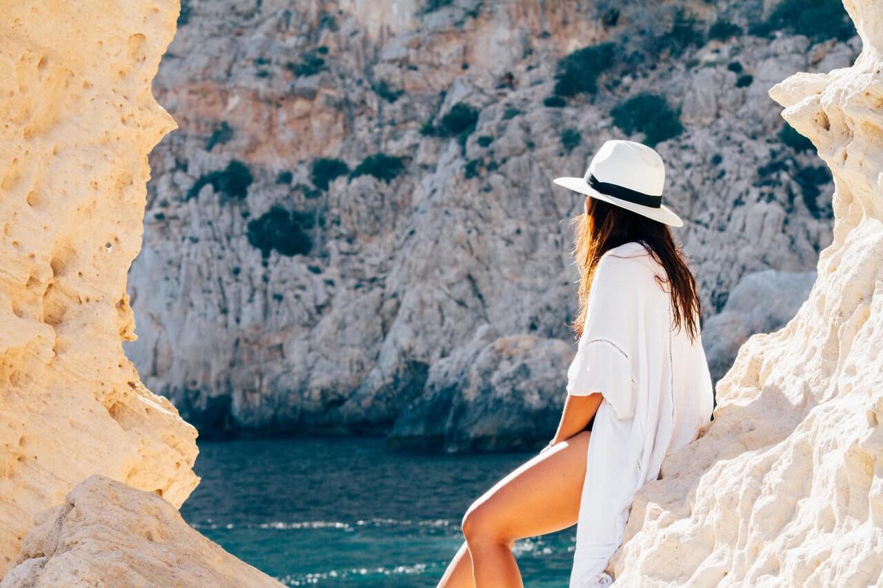 a person wearing a white hat and a white dress standing on a rocky cliff