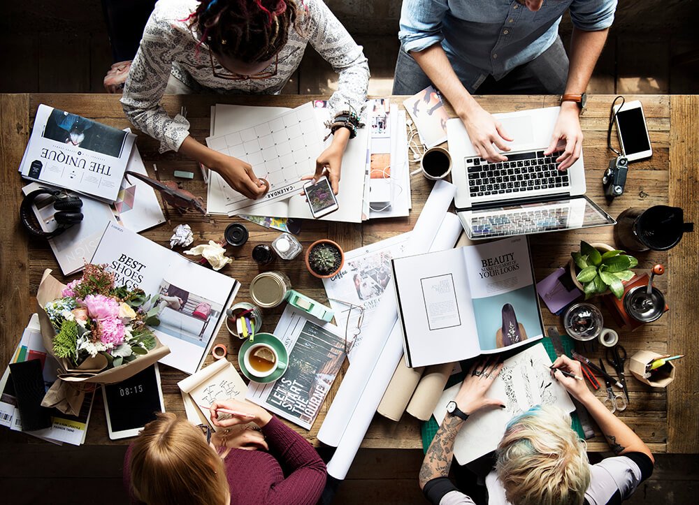 a group of people sitting around a table with a laptop and papers on it